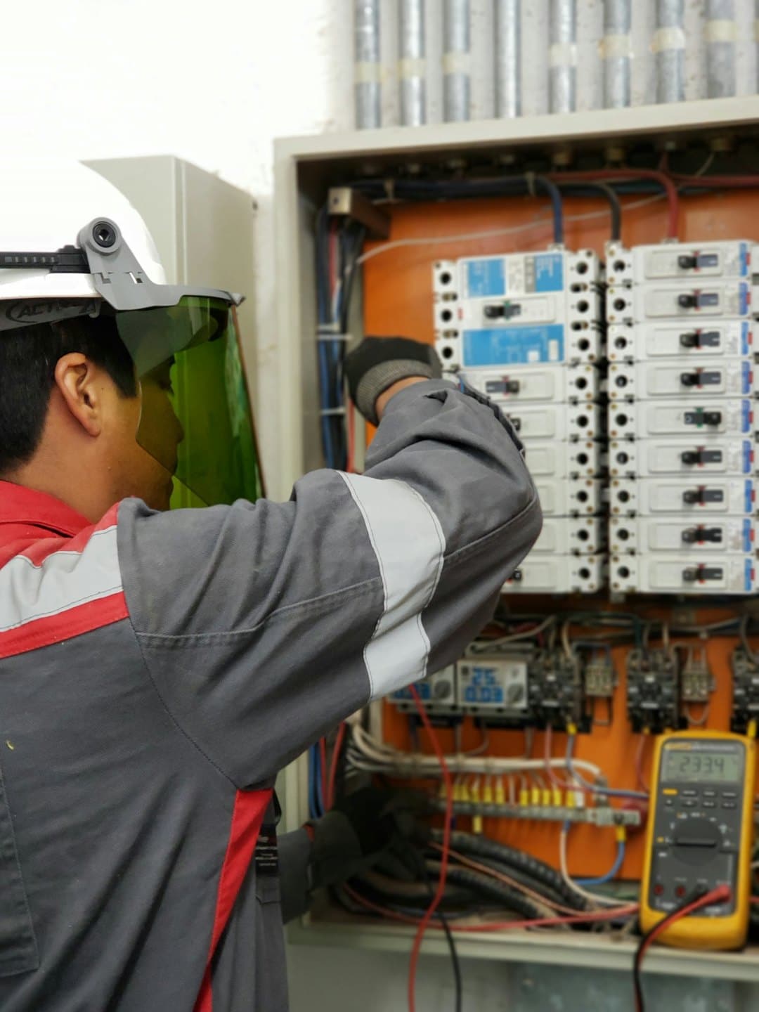 Teknisyen, devre kesiciler ve kablolarla açık bir elektrik panosunu inceliyor.