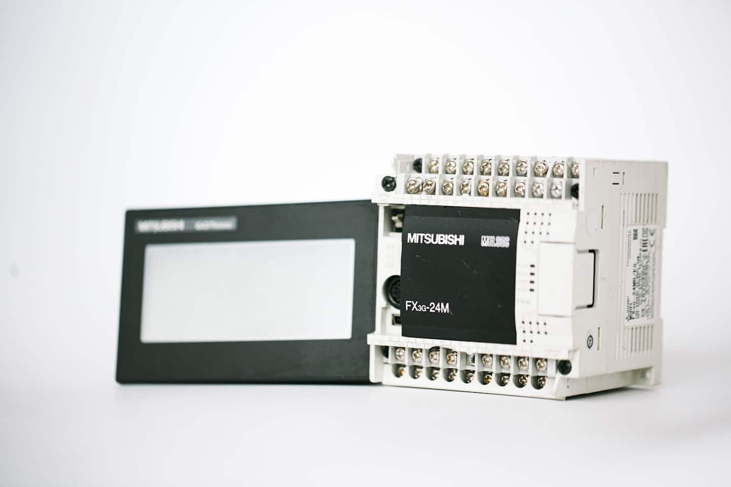 Beyaz bir yüzey üzerinde düzenlenmiş endüstriyel PLC ve HMI ekranı.